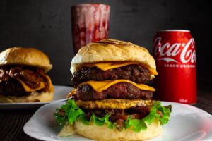 Close-up of a double cheeseburger with a Coca-Cola can, showcasing delicious layers of meat and cheese.
