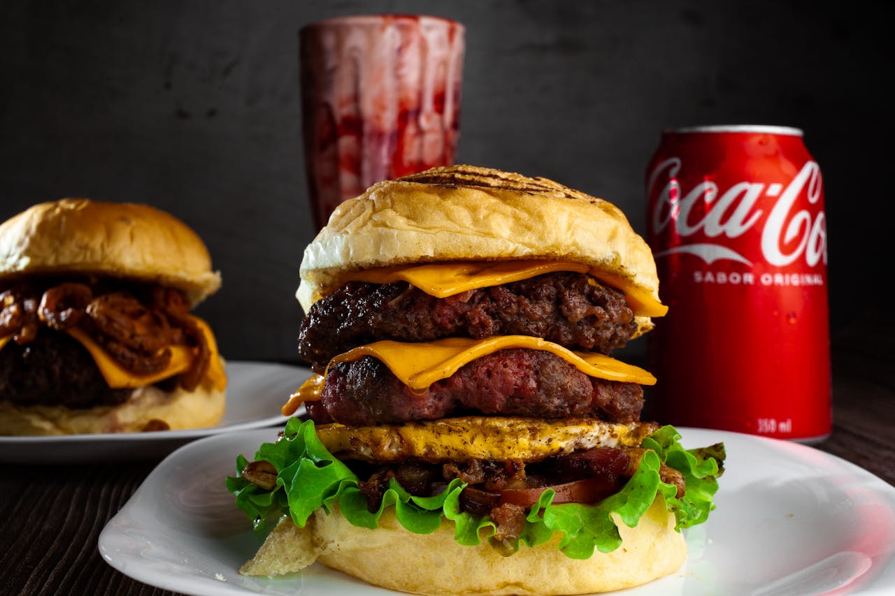 Close-up of a double cheeseburger with a Coca-Cola can, showcasing delicious layers of meat and cheese.