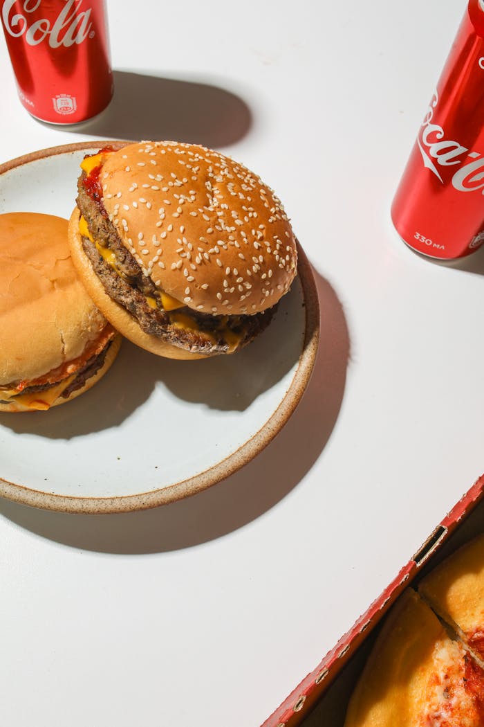 Top view of delicious cheeseburgers with Coca-Cola cans on a white table.