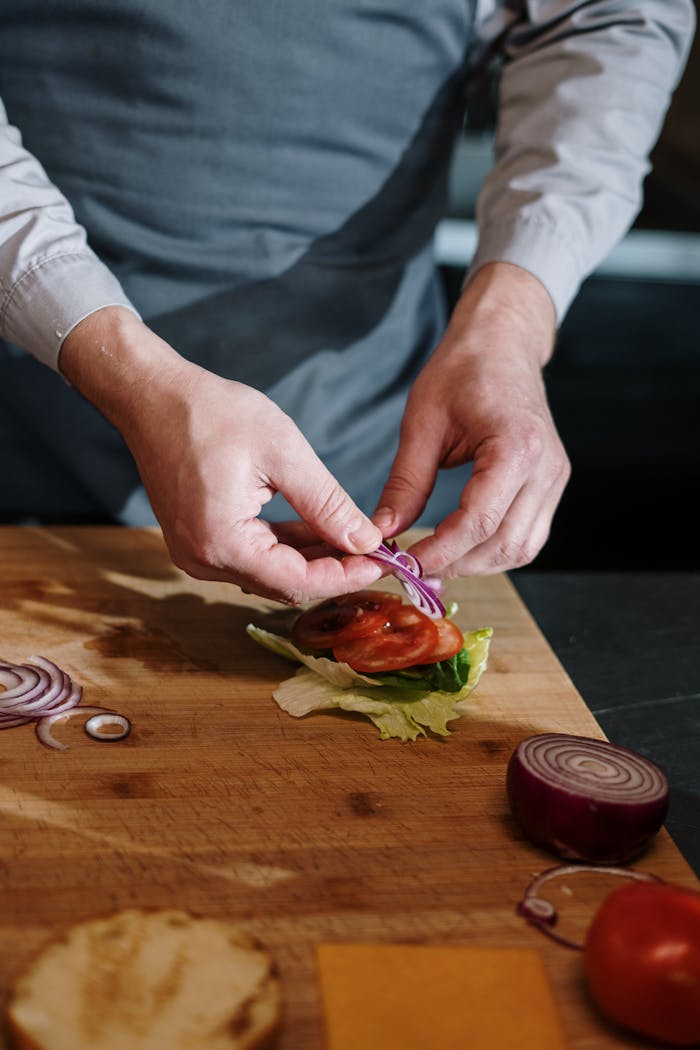 Chef assembling a vegetable sandwich with fresh ingredients, including tomatoes and red onions, in a kitchen setting.
